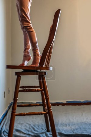 Junges Mädchen auf einem Stuhl, der hoch reicht, um eine Wand zu bemalen. Hochwertiges Foto