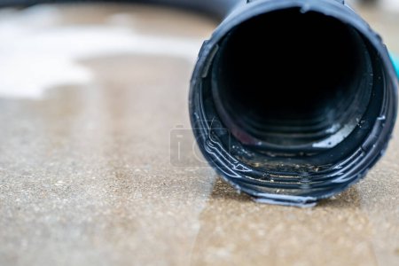 Selective focus on the front opening of a residential sump pump discharging water from the end of a flexible black hose. High quality photo
