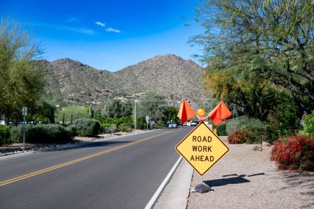 Road Work Ahead sign and flags posted on a road with construction in the background. . High quality photo
