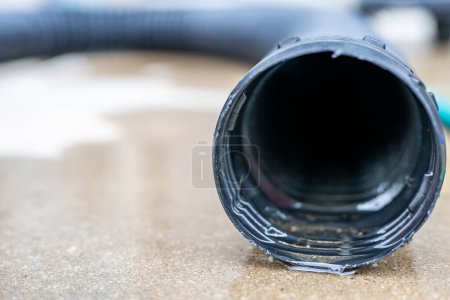 Enfoque selectivo en la abertura frontal de una bomba de sumidero residencial que descarga agua desde el extremo de una manguera negra flexible. Foto de alta calidad
