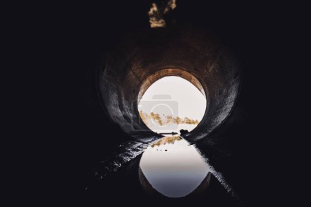 A dark tunnel extends into the distance, its walls reflecting in the murky water below. The tunnels arches create a unique visual effect, blending reality with the distorted illusion in the water.