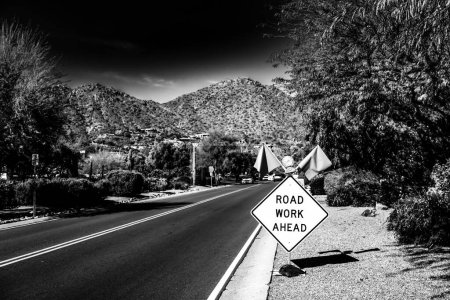 Road Work Ahead sign and flags posted on a road with construction in the background. . High quality photo