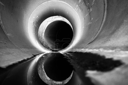 A black and white photograph of a pipe, the industrial subject stands out against a plain background. The textured surface and cylindrical shape are prominent in this stark image.