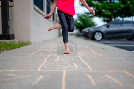 Selektiver Fokus auf Kreidezahlen mit einem Mädchen, das barfuß Hop-Scotch spielt. Hochwertiges Foto