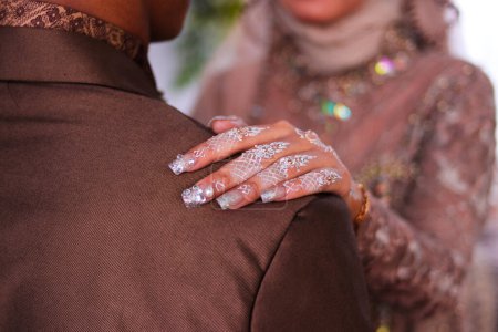 Foto de Vista de cerca de la novia musulmana asiática con arte de uñas blancas y hermoso hijab sosteniendo el hombro de su marido. - Imagen libre de derechos