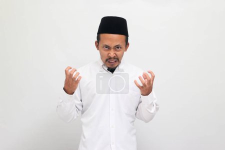 Téléchargez les photos : Un jeune Indonésien en colère portant une chanson ou peci ou kopiah, crie et crie avec une expression agressive, les bras levés, isolé sur un fond blanc - en image libre de droit