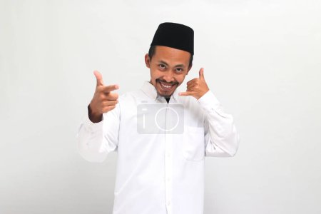 Téléchargez les photos : Jeune Indonésien excité portant une chanson ou peci ou kopiah, fait un geste de m'appeler tout en pointant vers la caméra, isolé sur un fond blanc - en image libre de droit
