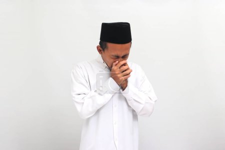 Téléchargez les photos : Malheureux jeune Indonésien portant une chanson ou peci ou kopiah, éternue souffrant de fièvre et la grippe, isolé sur un fond blanc - en image libre de droit