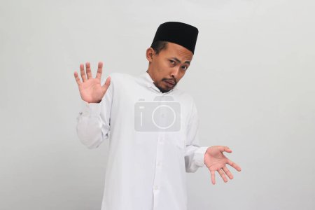 Téléchargez les photos : C'est dégueulasse. un Indonésien agacé, portant une chanson, un peci ou une kopiah, est repoussé par quelque chose, affichant une expression dégoûtée, isolé sur un fond blanc - en image libre de droit