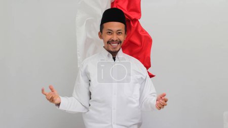 Téléchargez les photos : Un jeune Indonésien souriant, portant une chanson, un peci ou une kopiah, célèbre la fête de l'indépendance indonésienne le 17 août tout en se tenant debout sur le fond du drapeau indonésien, isolé sur fond blanc - en image libre de droit