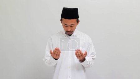 Téléchargez les photos : Un jeune homme politique indonésien, portant une chanson, un peci ou une kopiah, prie avant l'élection dans l'espoir de gagner, isolé sur fond blanc - en image libre de droit