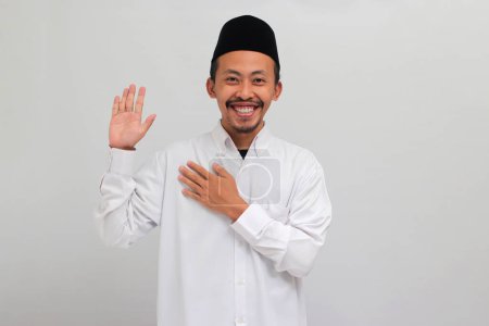 Téléchargez les photos : Un jeune Indonésien, vêtu d'une chanson, d'un peci ou d'une kopiah, jure la main sur la poitrine et la paume ouverte, prêtant serment de fidélité, isolé sur fond blanc - en image libre de droit