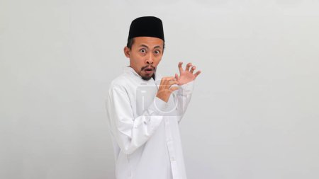 Téléchargez les photos : Jeune Indonésien effrayé, portant une chanson, peci, ou kopiah, a la bouche ouverte, l'air surpris et choqué, réagissant à quelque chose d'horrible, isolé sur fond blanc - en image libre de droit
