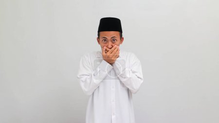 Téléchargez les photos : Choqué Jeune Indonésien, portant une chanson, peci, ou kopiah, couvrant sa bouche, sans voix, en entendant une rumeur ou des nouvelles inattendues, isolé sur fond blanc - en image libre de droit