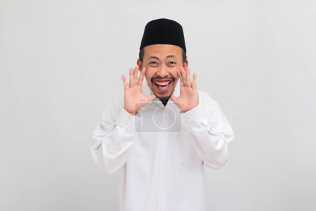 Téléchargez les photos : Un jeune Indonésien excité, portant une chanson, un peci ou une kopiah, tient sa main près de sa bouche et chuchote un secret, isolé sur fond blanc - en image libre de droit