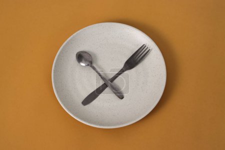Assiette vide avec cuillère et fourchette sur fond jaune, représentant le jeûne pendant le Ramadan et l'anticipation de la rupture du jeûne