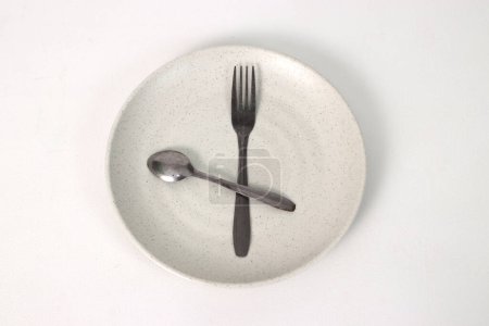 Empty plate with spoon and fork on a white background, representing fasting during Ramadan and the anticipation of breaking fast