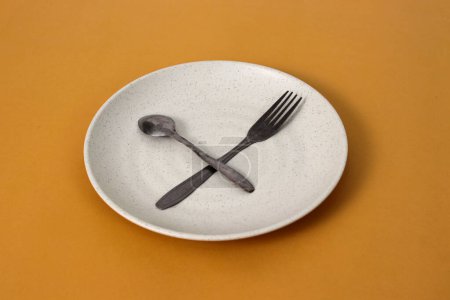 Empty plate with spoon and fork on a yellow background, representing fasting during Ramadan and the anticipation of breaking fast