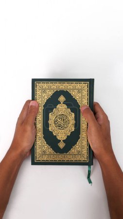 An Indonesian Muslim man holding the holy book of the Quran on a white background