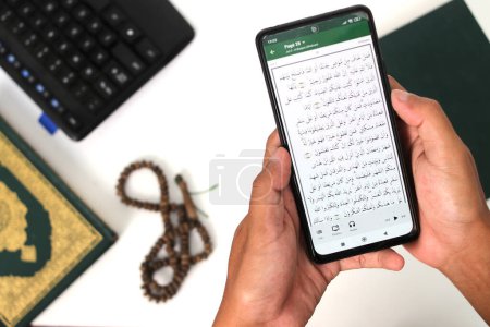 Photo for Indonesian Muslim worker taking a break to recite the Holy Quran on his phone during Ramadan - Royalty Free Image