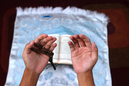 Indonesian man opening his palms in prayer after reciting the Quran on a prayer mat during Ramadan in the mosque
