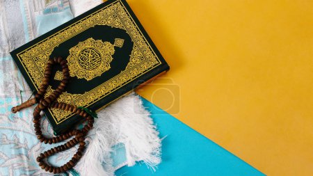 The Holy Quran with a prayer mat and tasbih on a blue and yellow background