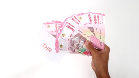 Hand holding a THR envelope filled with Indonesian Rupiah banknotes. THR or Tunjangan Hari Raya is a holiday allowance or bonus traditionally given to employees and those in need near during Ramadan