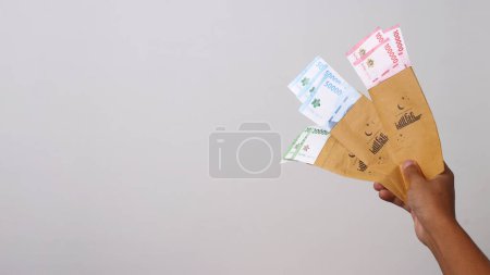 Mano sosteniendo un sobre THR lleno de billetes de Rupiah indonesios. THR o Tunjangan Hari Raya es un subsidio de vacaciones o bono que tradicionalmente se da a los empleados y los necesitados cerca durante el Ramadán.