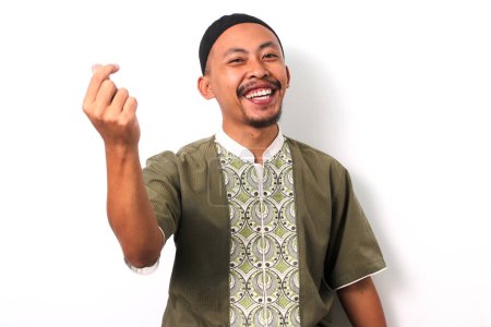 Un homme musulman indonésien souriant en chemise koko et peci fait un mini geste de c?ur avec ses doigts, exprimant amour et affection. Fond blanc.