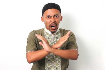 Téléchargez les photos : Homme musulman indonésien en chemise koko et peci crie avec les bras croisés dans un geste d'arrêt puissant. Isolé sur fond blanc - en image libre de droit