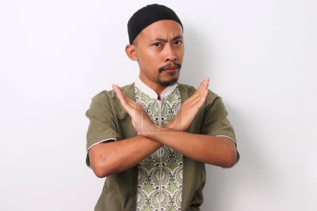 Téléchargez les photos : Homme musulman indonésien en chemise koko et peci croise les bras dans un geste d'arrêt. Isolé sur fond blanc - en image libre de droit