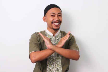 Téléchargez les photos : Homme musulman indonésien en chemise koko et peci croise les bras dans un geste d'arrêt. Isolé sur fond blanc - en image libre de droit