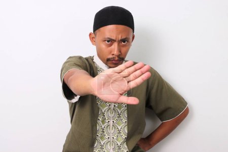 El musulmán indonesio con camisa koko y peci cruza sus brazos en un gesto de stop. Aislado sobre fondo blanco