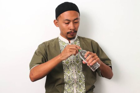Un musulman indonésien à Koko et peci brise son jeûne du Ramadan avec une bouteille d'eau minérale au coucher du soleil