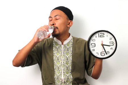 Ein indonesischer muslimischer Mann in Koko und Peki trinkt nach seiner sahur Mahlzeit Mineralwasser, um sich auf sein Ramadan-Fasten vorzubereiten. Isoliert auf weißem Hintergrund