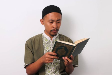 An Indonesian Muslim man reciting the Holy Quran with focus during Ramadan. Isolated on a white background