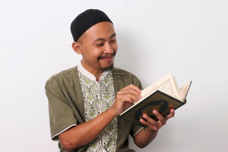 Photo for An Indonesian Muslim man reciting the Holy Quran with focus during Ramadan. Isolated on a white background - Royalty Free Image