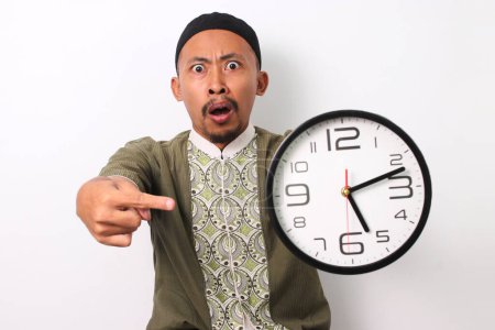 Ein schockierter indonesischer Muslim in Koko und Peci zeigt nachdrücklich auf eine Uhr und merkt, dass er während des Ramadan zu spät zum Sakur-Essen kommt. Isoliert auf weißem Hintergrund