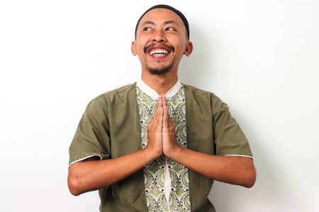 Ein fröhlicher indonesischer muslimischer Mann in Koko und Peci lächelt und gestikuliert zur Begrüßung des Ramadan den traditionellen Eid Mubarak-Gruß. Isoliert auf weißem Hintergrund