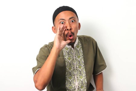 An Indonesian Muslim man in koko and peci cups his hand near his mouth in a gesture of announcement or sharing information. Isolated on a white background
