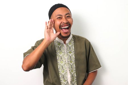 An Indonesian Muslim man in koko and peci cups his hand near his mouth in a gesture of announcement or sharing information. Isolated on a white background
