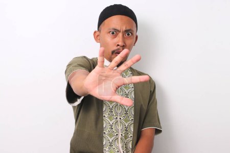 Ein indonesischer Muslim in Koko und Peci macht eine Stoppgeste und demonstriert sein Engagement, Verbote während des heiligen Monats Ramadan zu vermeiden. Isoliert auf weißem Hintergrund