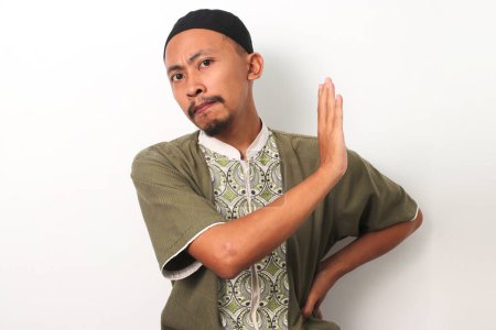 An Indonesian Muslim man in koko and peci makes a stop gesture, demonstrating his commitment to avoiding prohibitions during the holy month of Ramadan. Isolated on a white background