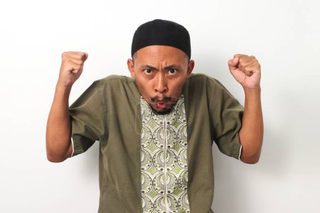 An Indonesian Muslim man, raises his fist in surprise and excitement upon receiving an unexpected offer during the special Ramadan period. Isolated against white background