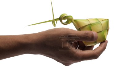 Hand presenting a ketupat pouch, a traditional Indonesian dish made from woven young coconut leaves (janur), isolated on white background