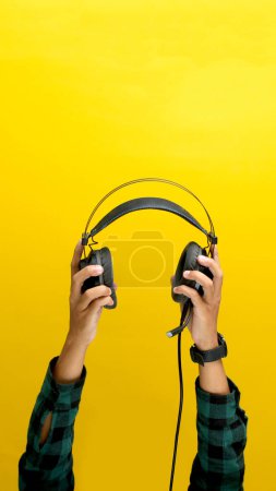 La main saisit un casque noir sur un fond jaune vif. Idéal pour illustrer des concepts tels que l'écoute de musique, l'équipement audio ou la technologie du son.
