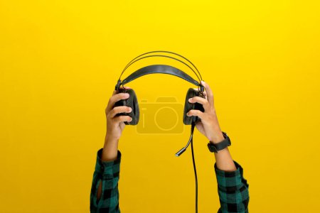 Mano agarra un auricular negro sobre un fondo amarillo brillante. Ideal para ilustrar conceptos como escuchar música, equipos de audio o tecnología de sonido.