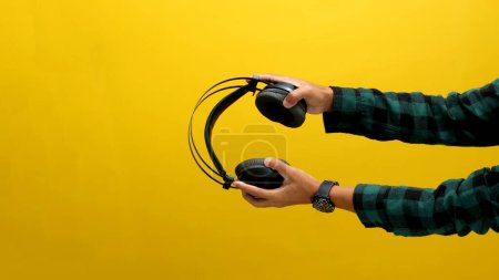 Mano agarra un auricular negro sobre un fondo amarillo brillante. Ideal para ilustrar conceptos como escuchar música, equipos de audio o tecnología de sonido.