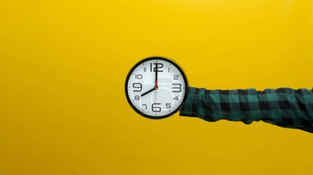 Zeiger, der eine Wanduhr vor einem leuchtend gelben Hintergrund hält. Ideal zur Darstellung von Zeitmanagement, Erinnerungen oder dem Konzept des Countdowns.