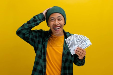 Aufgeregte Asiaten in Mütze und lässiger Kleidung halten Geldscheine in der Hand. Vereinzelt auf leuchtend gelbem Hintergrund. Perfekt, um Konzepte von finanziellem Gewinn, Aufregung und Wohlstand zu illustrieren.